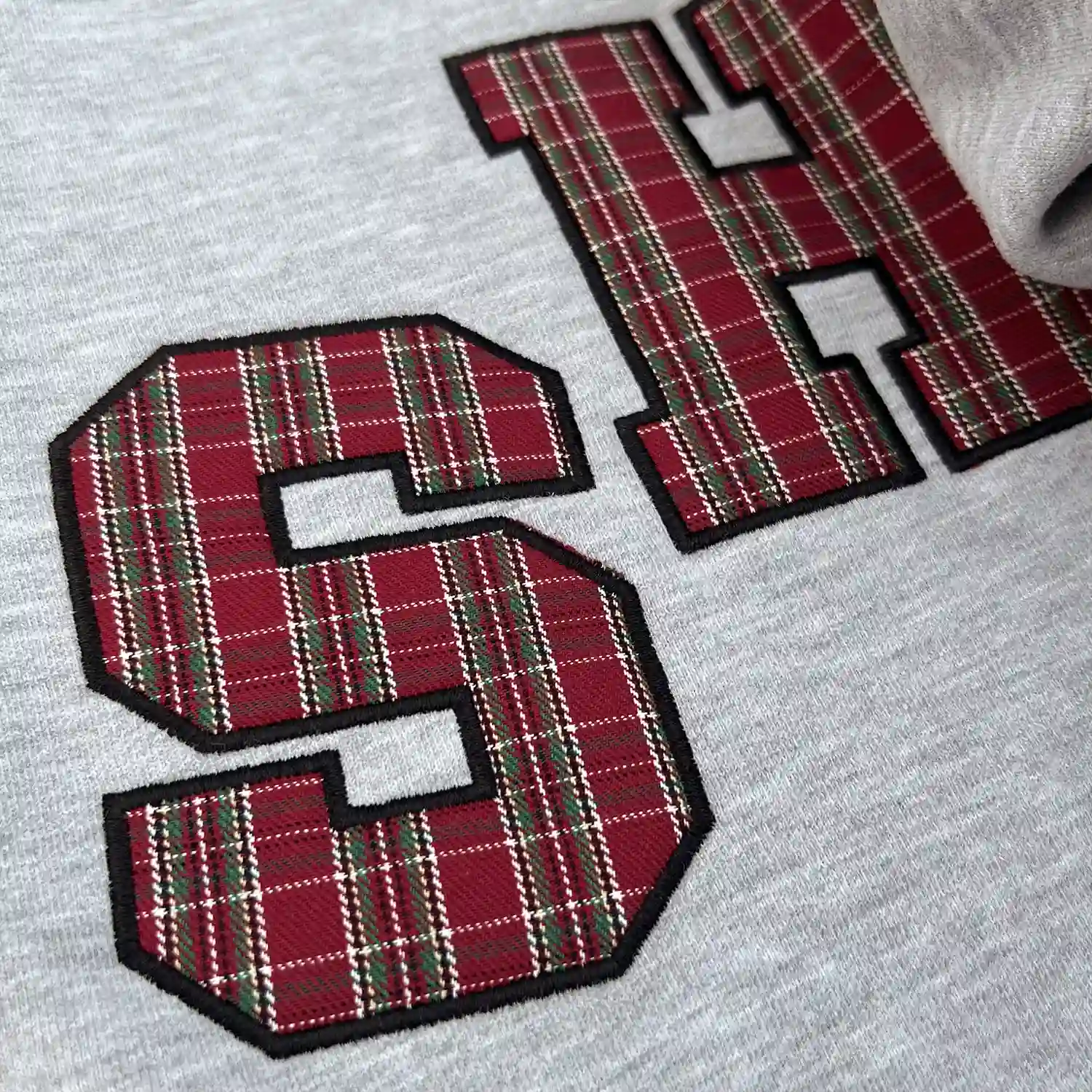 Macro view of high-density satin stitch embroidery and plaid fabric patch.