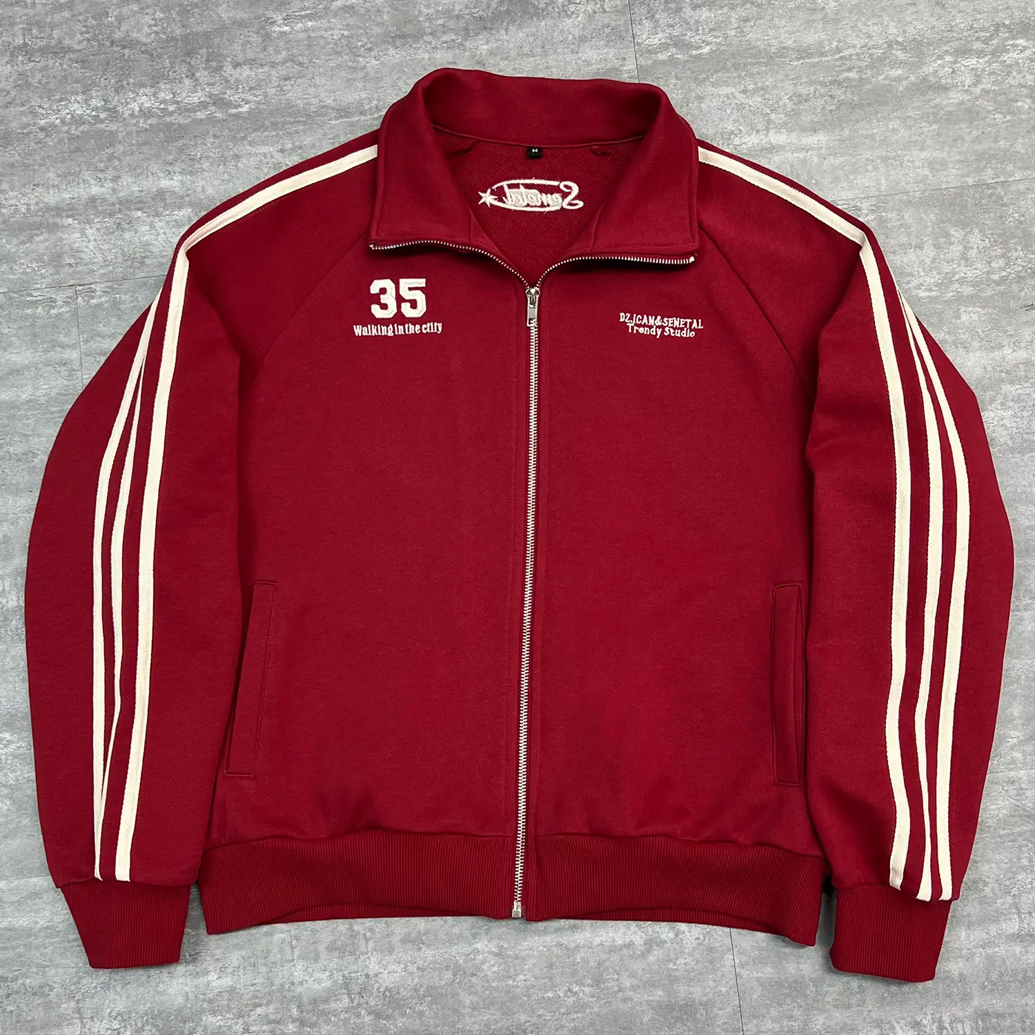 Front view of red custom track jacket with white side stripes and vintage embroidery.