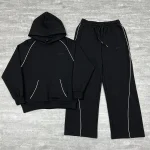 Front flat lay of the black custom piping tracksuit showing the raglan hoodie and wide-leg sweatpants.