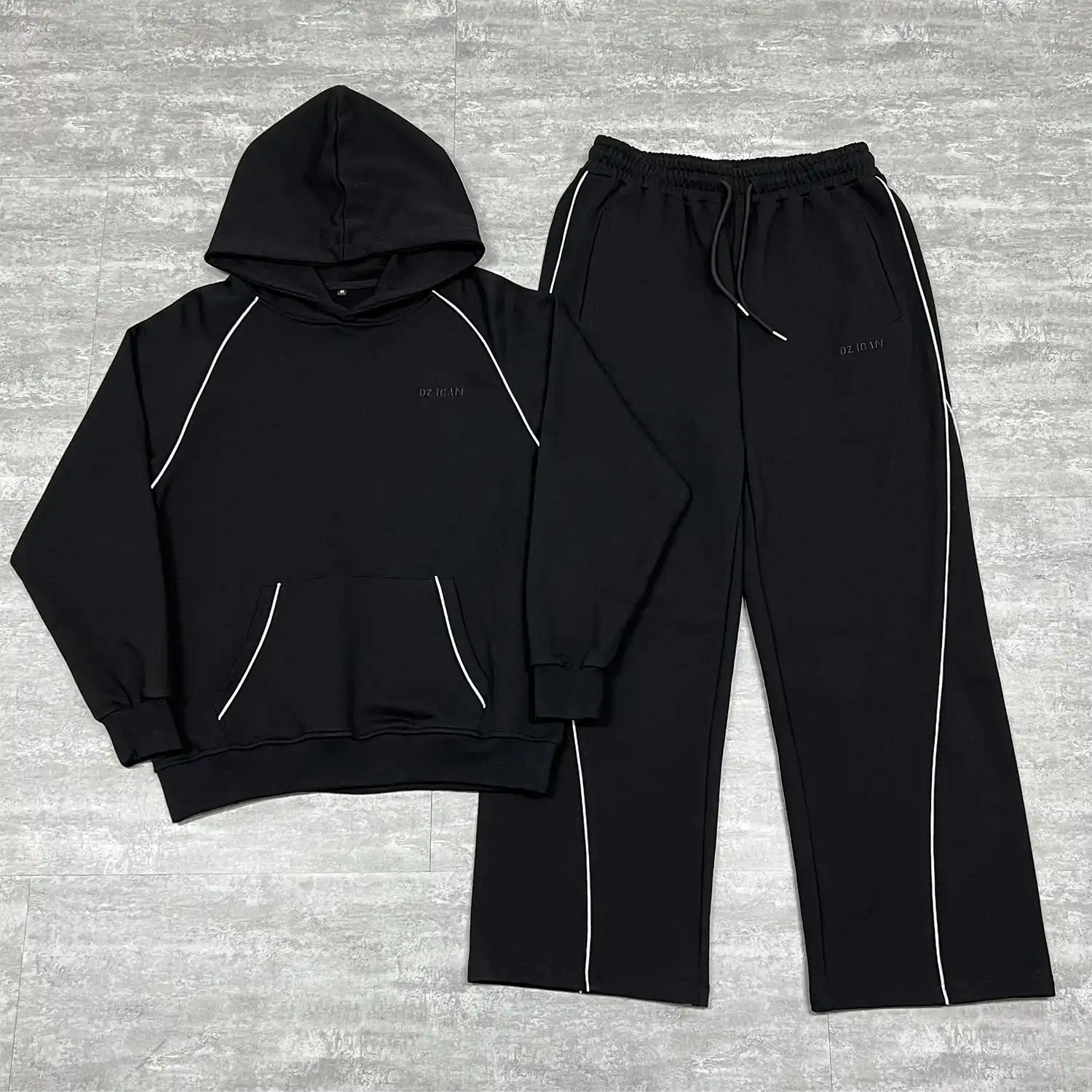 Front flat lay of the black custom piping tracksuit showing the raglan hoodie and wide-leg sweatpants.